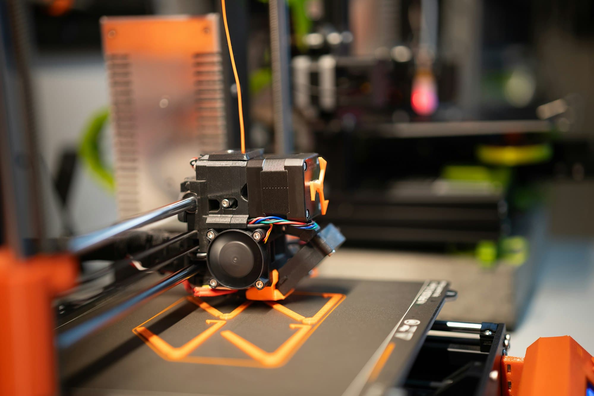 3D printer nozzle laying down the first layer of an orange part